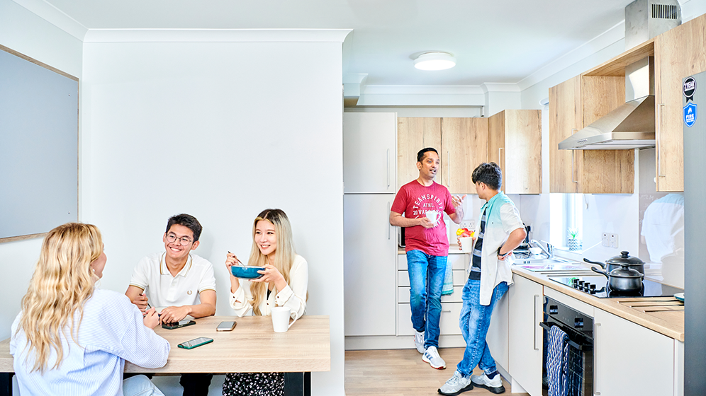 An alternative view of an open plan kitchen showing the breakfast bar. There are two windows and large, flat screen TV on the wall. 